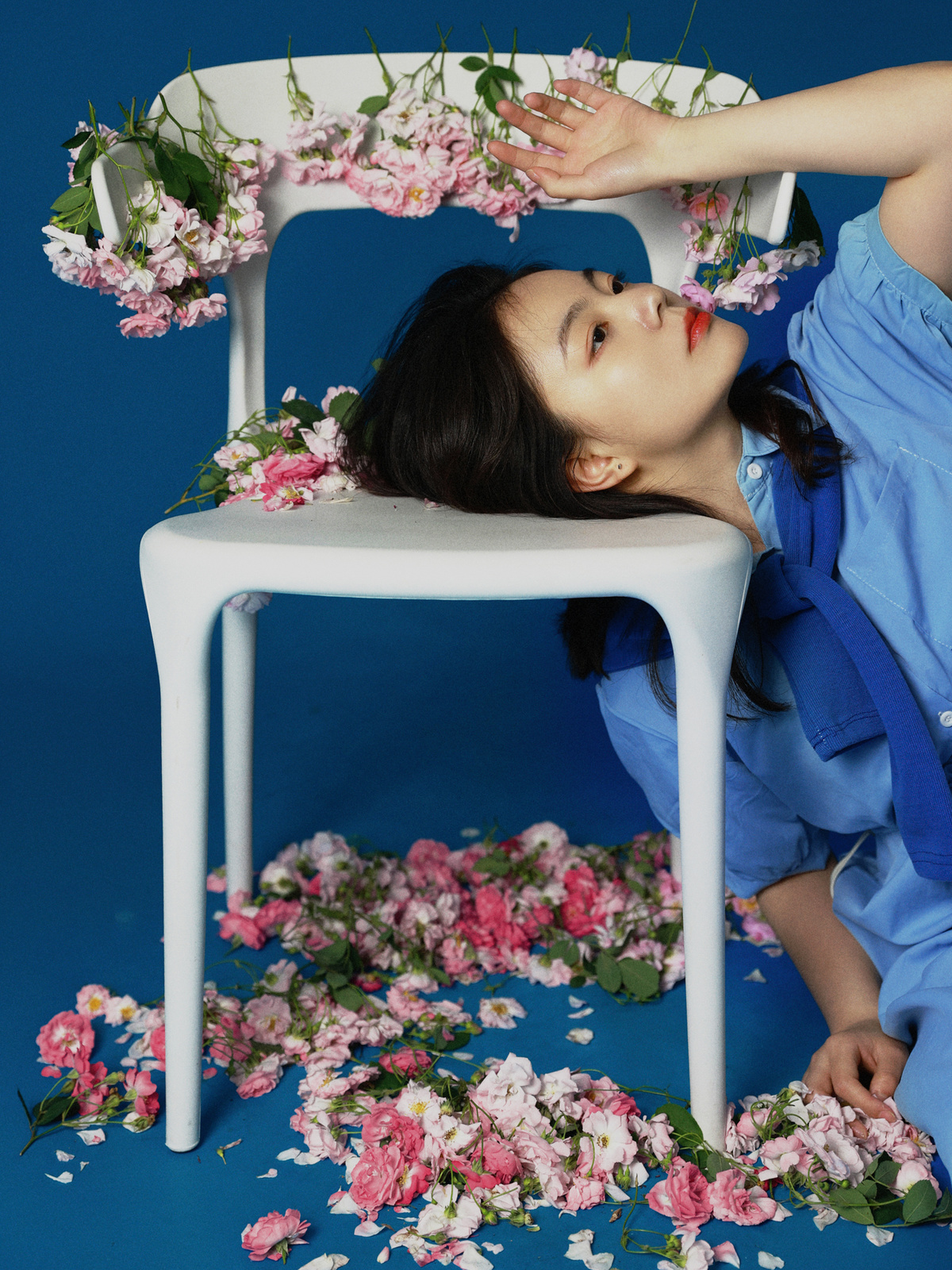 一位穿着蓝色连衣裙的年轻女子坐在白色椅子上 周围环绕着花。