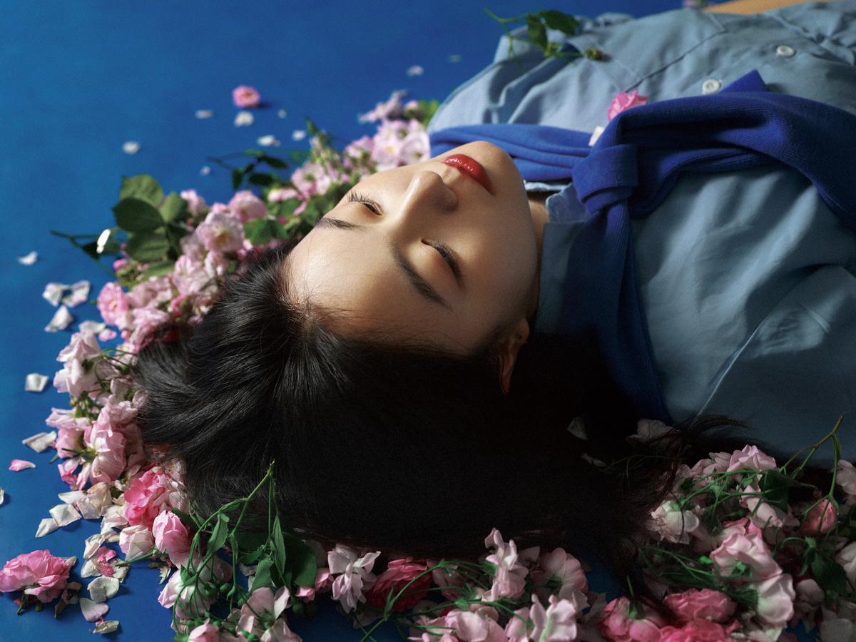 一个穿着蓝色连衣裙的年轻女子躺在花丛中的花瓣床上。