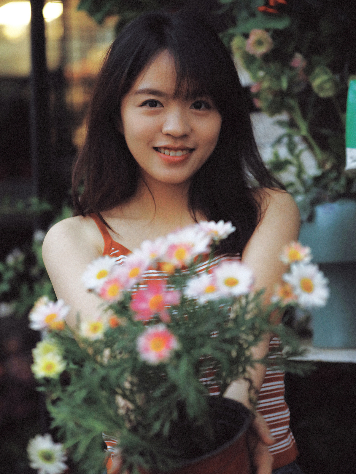 一位穿着连衣裙的年轻女子手持一束花站在一盆植物旁边