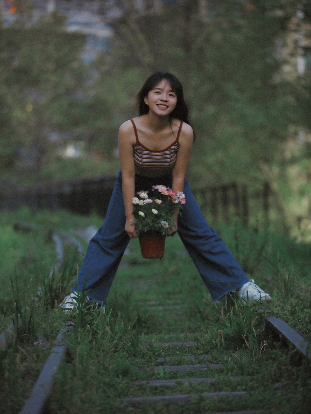 一位年轻女子抱着花盆在铁路轨道上摆姿势