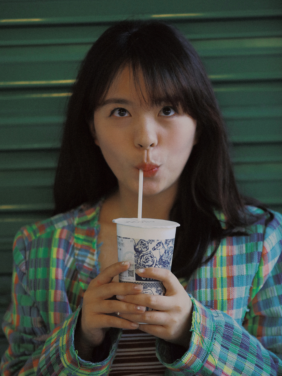 一个穿着格子衬衫的年轻女子正在用吸管喝着杯子里的饮料。
