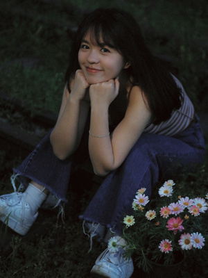 一位年轻女子坐在草地上 旁边有花。