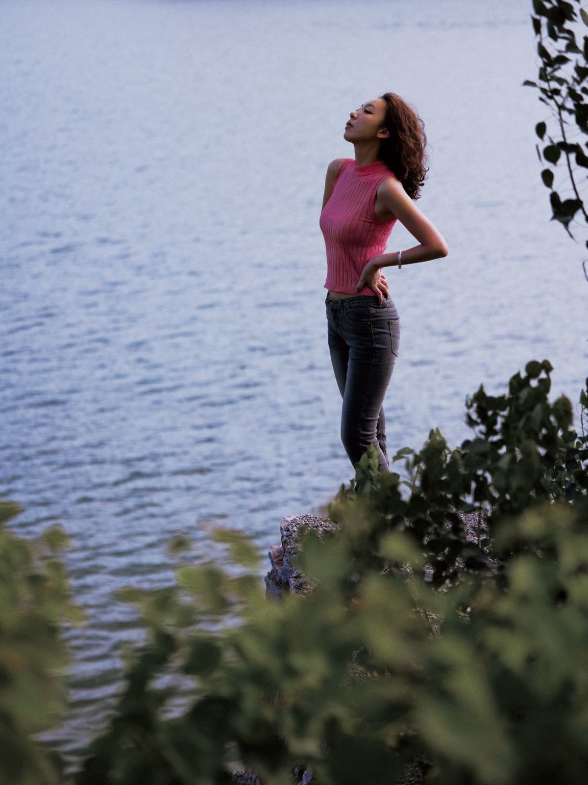 一位穿粉色衣服的年轻女子站在一块岩石上 眺望着湖泊。