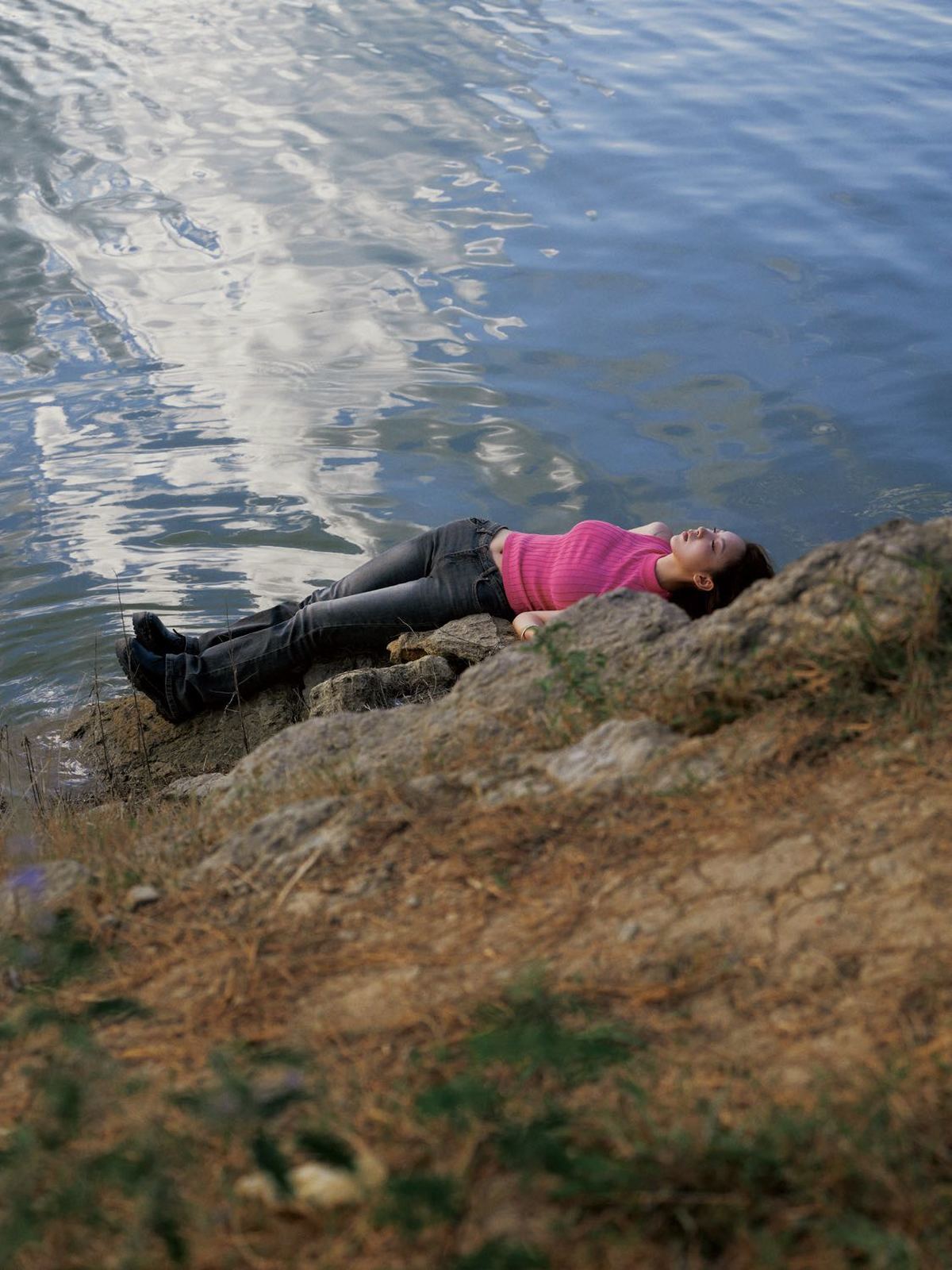 一位年轻女子躺在湖边或水体的岩石上