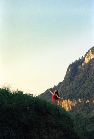 一位穿着红裙子的年轻女子站在绿草丛生的小山丘上 伸开双臂。