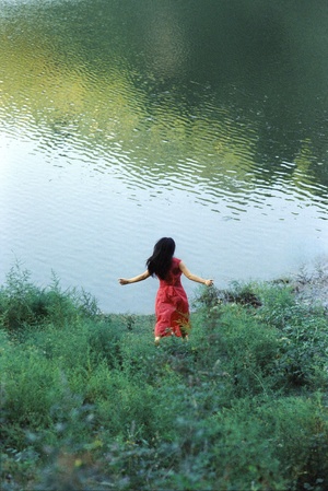 一位穿着红裙子的年轻女子沿着湖泊附近的水体走动。