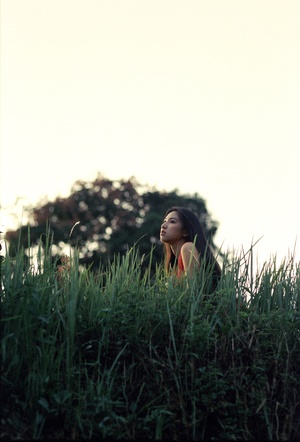一位年轻女子坐在草丛丛生的草地上 位于绿草茵茵的山顶。