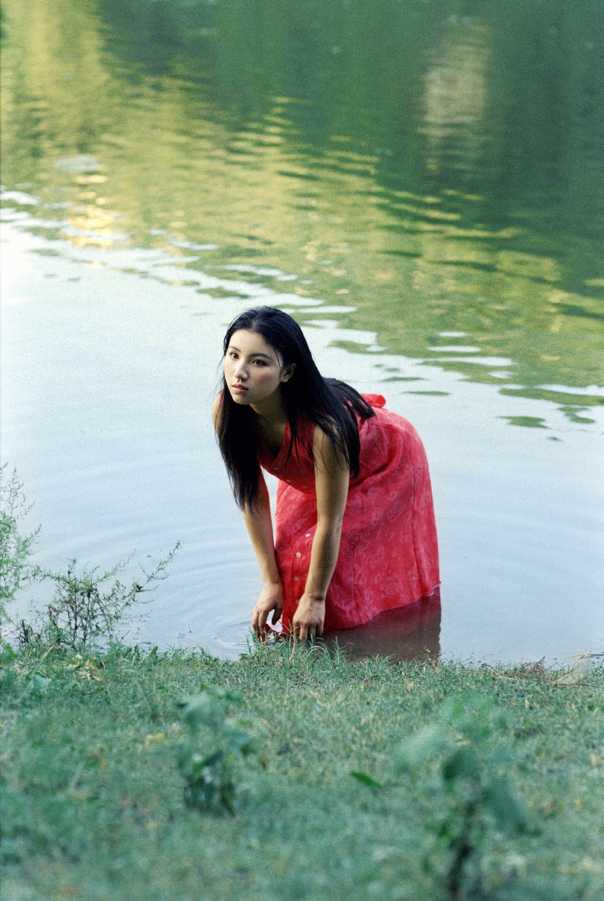 一位穿着红色连衣裙的年轻女子正在湖或河里涉水