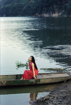 一位穿着红裙子的年轻女子坐在湖中的一艘小船上