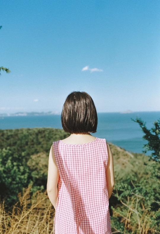 一个穿着粉色连衣裙的小女孩站在小山上眺望大海