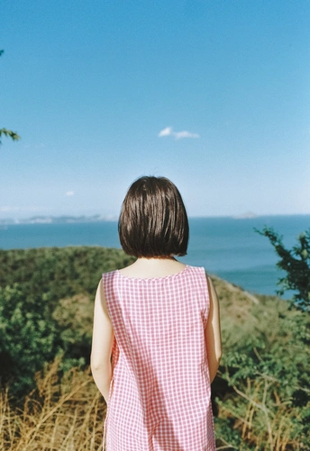 一个穿着粉色连衣裙的小女孩站在小山上眺望大海