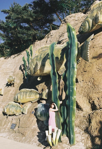 一位女士在一堵巨大的岩壁前摆姿势拍照 岩壁上有一条鱼和一些植物的雕像