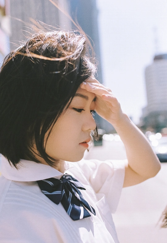 一位身穿白衬衫、打着领结的年轻女子低头看着背景是一座城市的街道