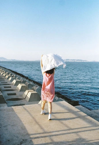 一个穿着粉色连衣裙、打着白色雨伞的小女孩站在水面上的码头上 而一个打着白色伞的人站在她的头上