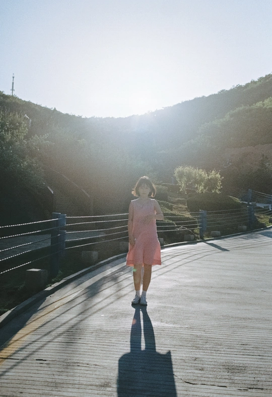 一个穿着粉色连衣裙的年轻女子走过一座木桥