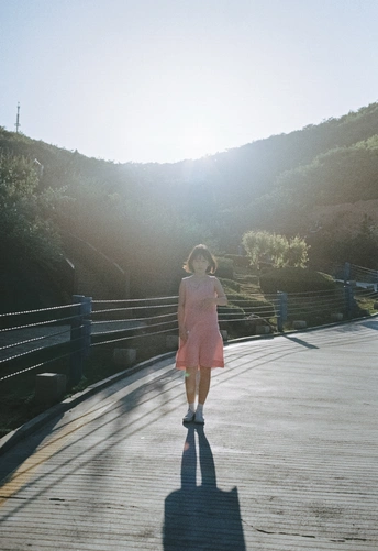 一个穿着粉色连衣裙的年轻女子走过一座木桥