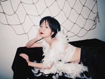 一个年轻女子坐在黑色沙发上 床上有白色的羽毛。