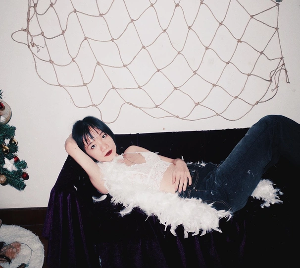 一个年轻女子躺在黑色沙发上 旁边有一棵白色的圣诞树。