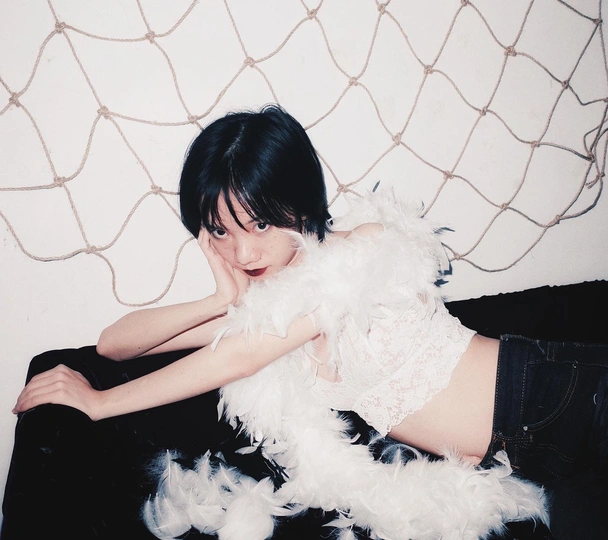 一个年轻女子坐在黑色沙发上 抱着一个白色毛绒玩具。