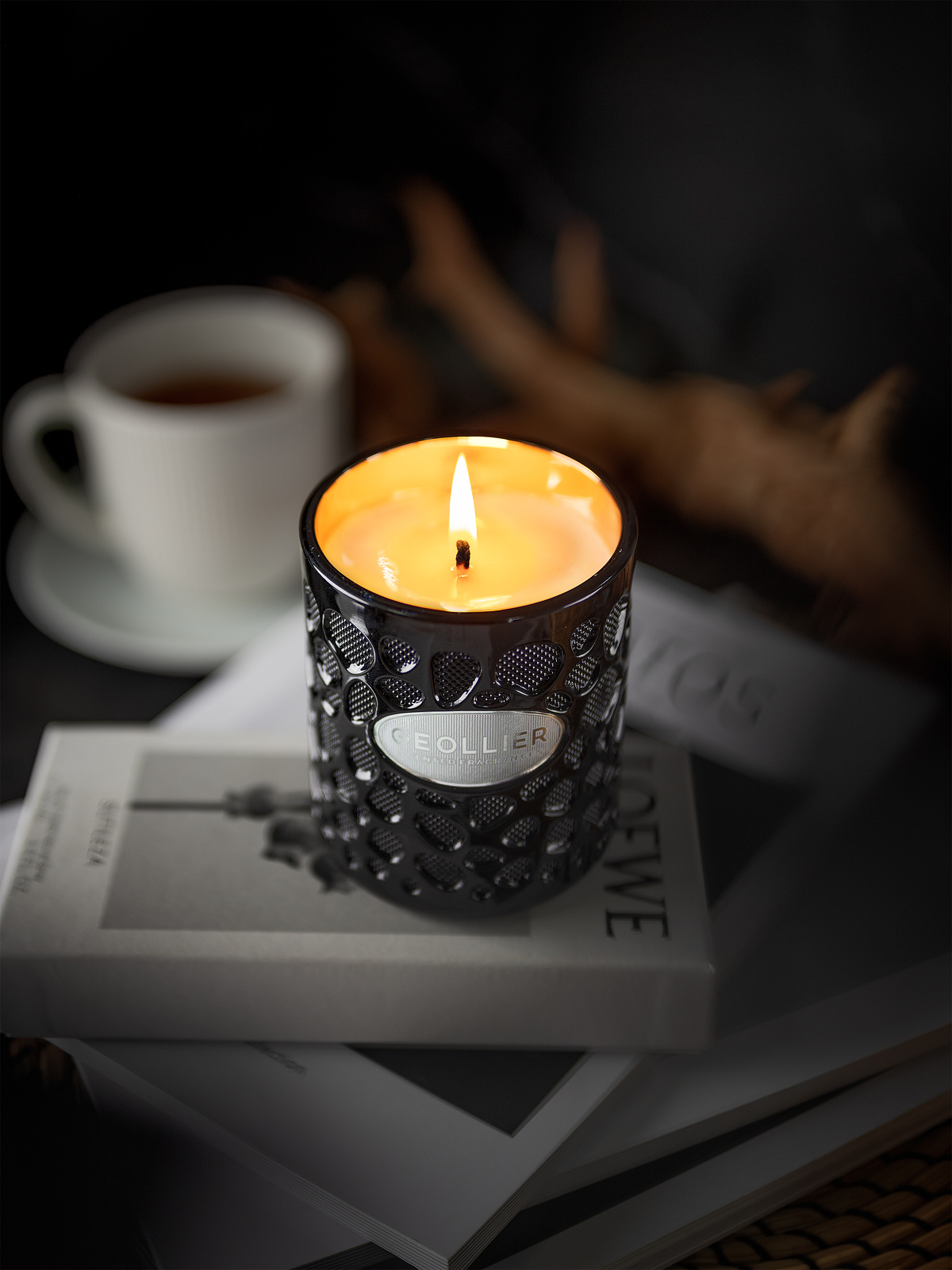 一支点燃的蜡烛坐在书旁边 旁边是一杯咖啡。