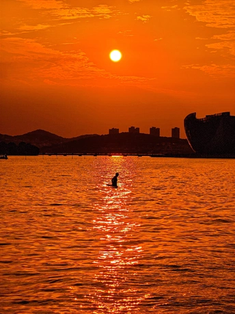 夕阳西下 背景是一座城市 中间有一艘船在大海上。