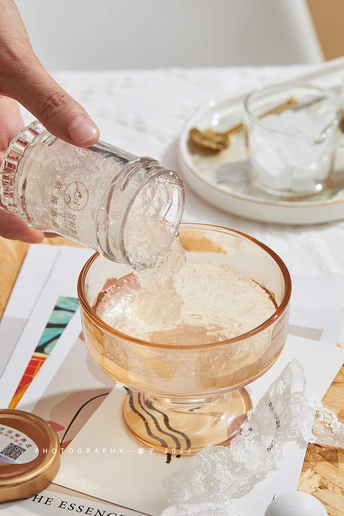 一个人正在往桌子上的一杯水中倒盐 旁边还有其他餐具和食材。