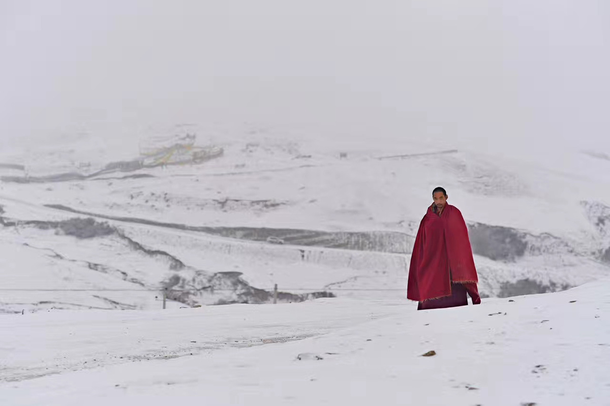 一个穿着红色长袍的男人走在背景是山脉的雪山上