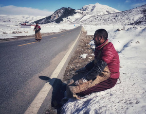 一个人坐在白雪皑皑的高速公路上 背景是雪山 前景是人