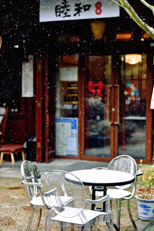 一个坐在餐厅外的男人 周围是雪 桌子和遮阳伞是白色的。