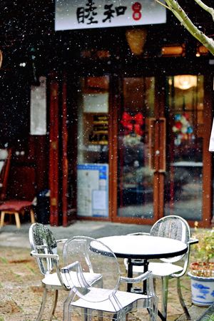 一个坐在餐厅外的男人 周围是雪 桌子和遮阳伞是白色的。