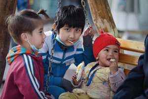 两个小男孩坐在游乐场的秋千上 其他年轻儿童在吃东西。