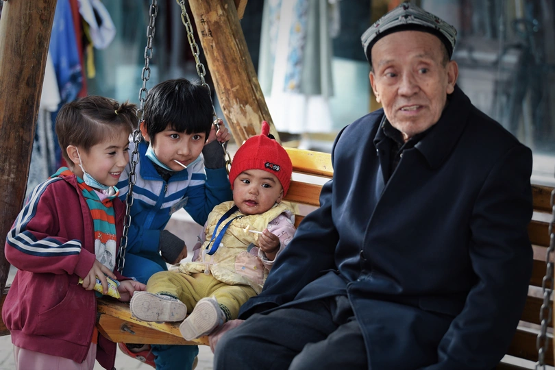 一个老人坐在木凳上 两个年轻的孩子坐在上面。