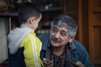 一个老人拿着锤子站在一个年轻男孩旁边