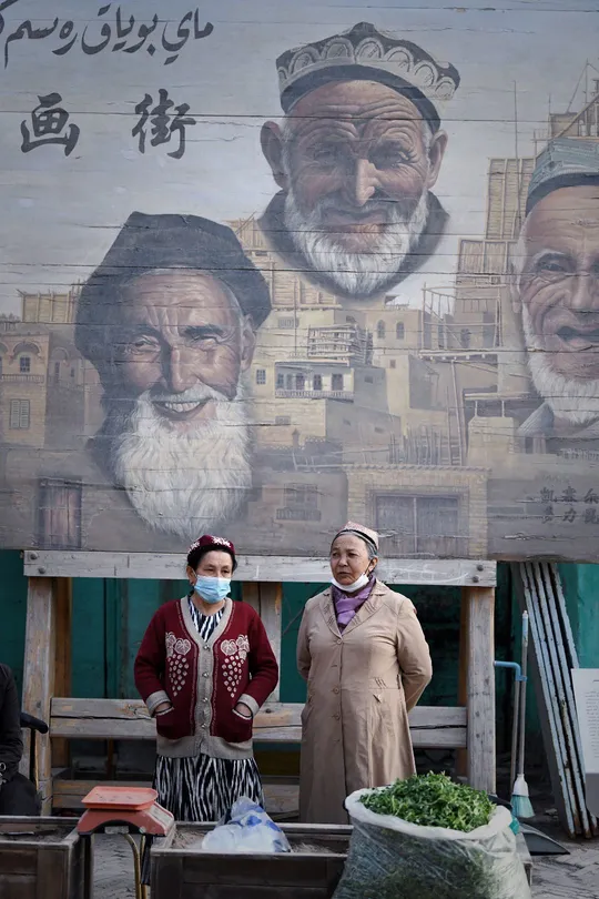 一个戴面具的男子走过一个戴口罩站在建筑物墙壁前大壁画前的女人。