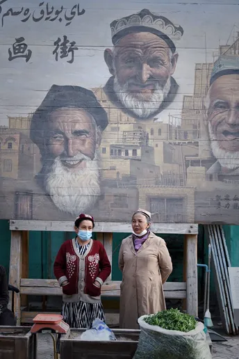 一个戴面具的男子走过一个戴口罩站在建筑物墙壁前大壁画前的女人。