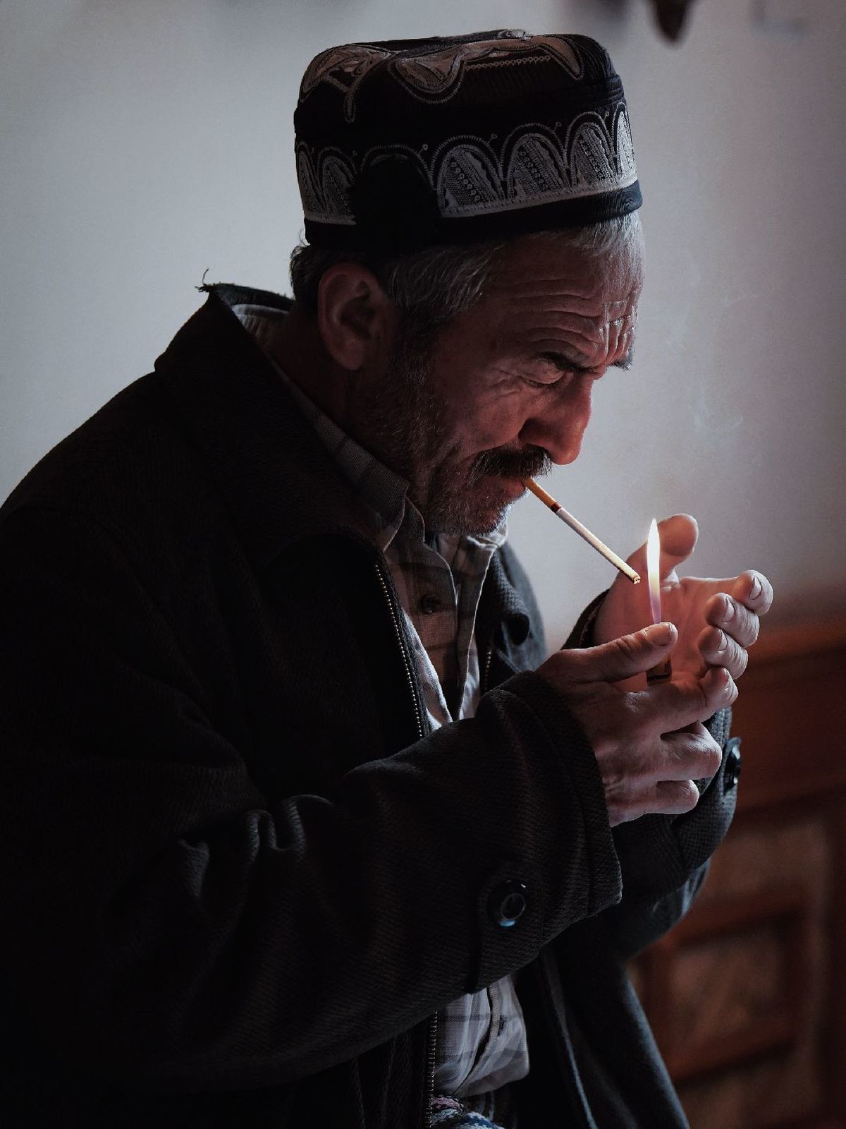 一个老人正在抽烟斗 手里拿着一支点燃的蜡烛。