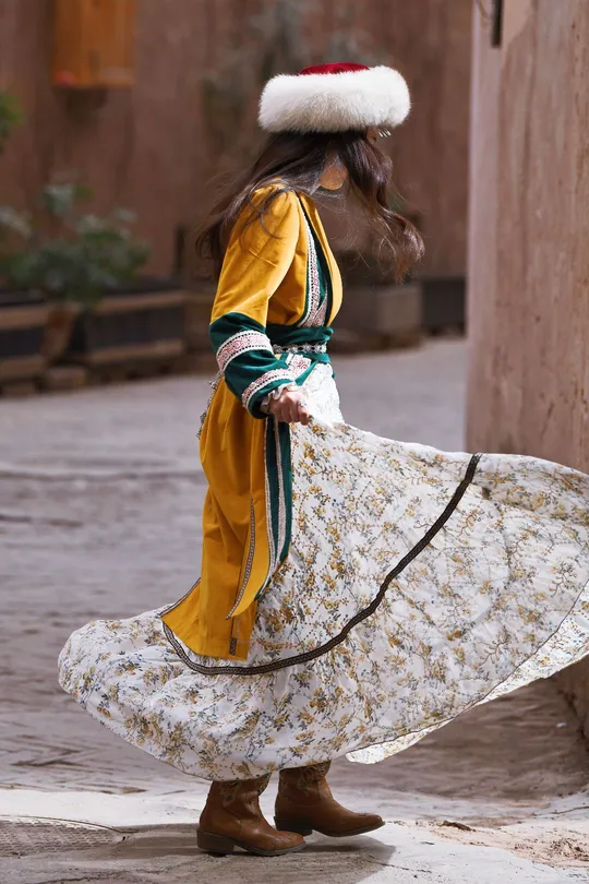 一位穿着传统服装的小女孩戴着帽子 拿着雨伞。