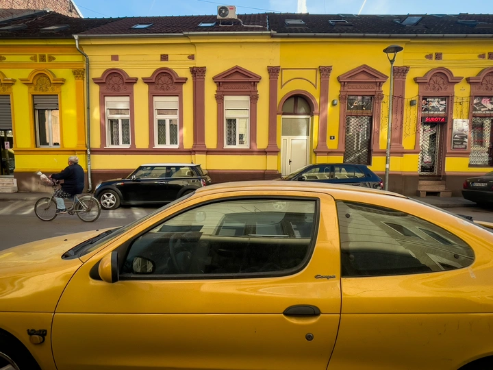 一辆黄色汽车在彩色建筑前驶过 一辆自行车停在它前面。