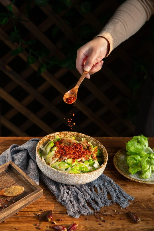 一位手里拿着勺子的女士正在从木桌上的一碗沙拉中捞出沙拉 碗里有香料、 lettuce 和盐。