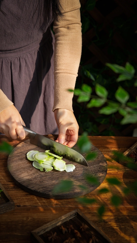 一位女性正在用刀在木板上切绿洋葱 而另一个人正在桌子上切一些蔬菜。