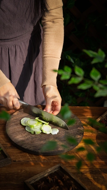 一位女性正在用刀在木板上切绿洋葱 而另一个人正在桌子上切一些蔬菜。