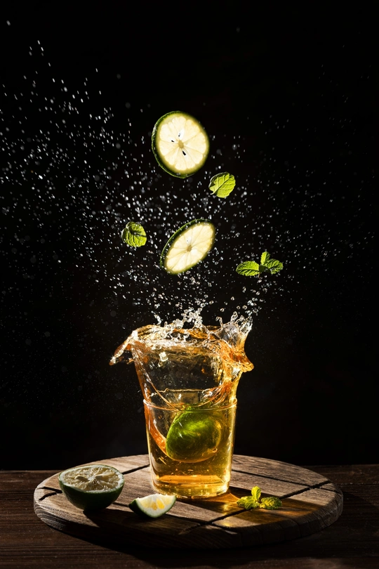 在一个带有冰的玻璃杯中溅起的水花 桌子上放着水果和柠檬 背景是黑色。