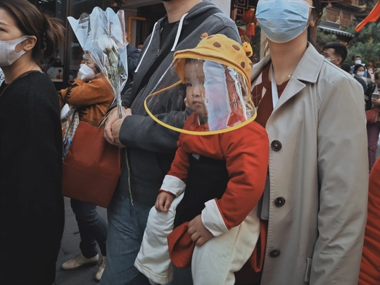 一名戴口罩的男子在香港街头抱着一个穿着女装的儿童 这是中新社图片。