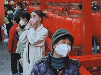 一些人戴着口罩站在一个红色的鸟居前面。