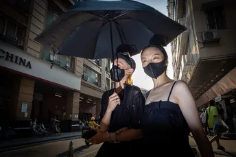 一些戴黑色面罩的女人站在遮阳伞下 人们走在街上。