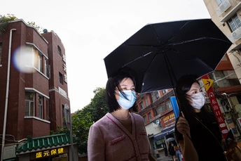 一位戴口罩的女人拿着一把黑色雨伞 在雨天城市街道上 人们正在走动。