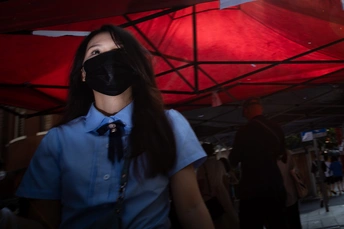 一位年轻女子穿着蓝色衬衫和领带站在红色帐篷下 脸上戴着黑色面具。