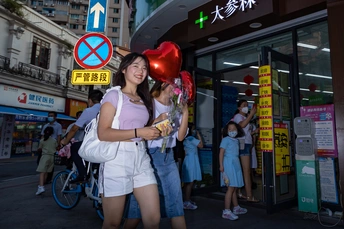 一位年轻女子手持花和气球站在街道上
