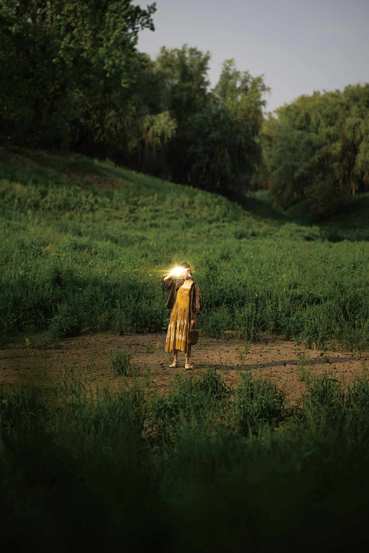 一个穿着黄色连衣裙的女人走在绿色田野的小路上