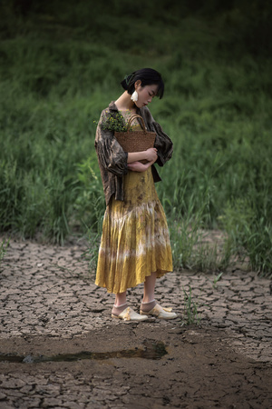 一个穿着黄色连衣裙的年轻女子提着一个小篮子穿过泥泞的田野